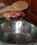 Hold half the pomagranate over the water and whack it strongly with a spoon to release the seeds.